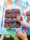 A child's hand reaching for a slice of chocolate and raspberry cake at a school fete