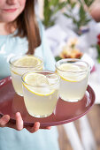 A girl holding three glasses of lemonade on a tray