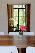 Solid wooden table and chairs with white backs in dining room in front of open doorway showing glass wall with view of garden