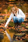 Frau an einem Bach im herbstlichen Wald