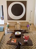Selbstgefertigter Couchtisch in künstlerischem Stil und moderne, sandfarbene Sofagarnitur vor modernem Bild an Wand