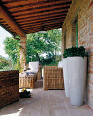 Terrakottageflieste Veranda eines toskanischen Landhauses mit gemütlichen Korbmöbeln; im Vordergrund zwei weiße Bodenvasen