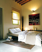 Schlafzimmer mit Betonestrich und Holzdielenboden; an der Wand ein modernes Gemälde und warmes Licht einer Wandleuchte