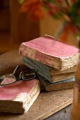 Historische, zerfledderte Bücher auf alter Holzplatte im Kontrast zu moderner Brille