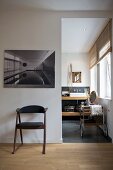 Elegant mixture of wood and grey elements - retro chair beneath black and white photograph next to doorway with view of contemporary ensuite bathroom