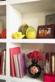 Weisses Bücherregal mit Rosenvase, gelben Glas-Eiern und gerahmtes Familienfoto