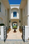 Sunny entrance with wrought iron gate, terra cotta tiles and small trees in square wooden planters