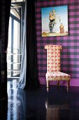 Chair with patterned upholstery fabric in front of a purple plaid wall with a modern painting