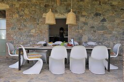 Mediterranean terrace dining area with white shell chairs and table against stone wall