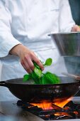 A chef adding spinach to a pan
