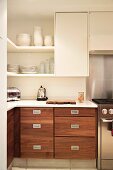 Corner of kitchen with crockery on shelving above base units with wooden doors