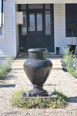 Brunnen in Form einer anthrazitfarbenen Amphore auf dem Kiesweg vor einer Hauseingangstür