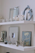 Metal sign, picture frames, shells and old perfume bottles decorating white shelves