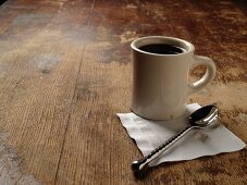 Tasse mit Kaffee auf Holzuntergrund mit Serviette und Löffel