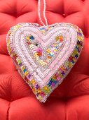 A fabric heart decorated with sequins on a red surface