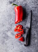 Eine rote Peperoni, angeschnitten, mit Messer
