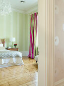 Schlafzimmer in zartem Grün mit einfachem Holzdielenboden und farbenfrohen Vorhängen mit pinkfarbenen Streifen