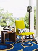 Yellow, upholstered chair on a modern rug with a distinct pattern on a veranda with Doric columns
