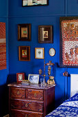 Yves Klein-Blau getönte Schlafzimmerecke mit antiker Kommode unter gerahmten Bildern
