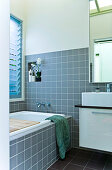 A bathroom with grey tiles, a small wall niche with a spotted pattern and a wooden, vintage-style shelf