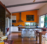 A spacious kitchen with a bright orange wall and a shiny kitchen counter with designer chairs