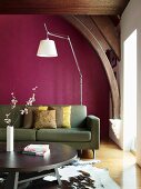 Modern couch in front of purple wall below historical ceiling beams; round coffee table on animal-skin rug in foreground