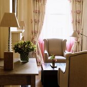 Tischlampe auf Tisch neben Loungeecke - Elegante Sessel und Kaffeetisch vor Fenster mit gerafften Vorhängen