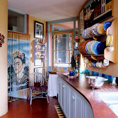 Kitchen counter below plates in wall-mounted plate rack opposite thread curtain with portrait of Frida Kahlo in doorway