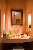 Simple washstand in niche with sunken, brass sink and framed mirror on wall