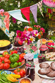 A table laid in a garden with biscuits, fresh vegetables, jam and cake