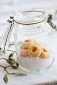 Sugar and shortbread jam biscuits in a flip top jar with a sprig mistletoe in front of it