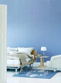 Bedside table and modern armchair in front of blue-painted wall