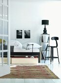 Bed and high, black-painted wooden stool with backrest in minimalist bedroom
