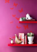 Rot lackierte Regalböden vor lila getönter Wand mit Schmetterlingmotiven