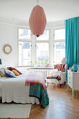 Bright bedroom with double bed below pendant lamp and comfortable armchair in bay window