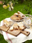 A baguette on a chopping board and other types of bread in a bread basket on a table in the open air