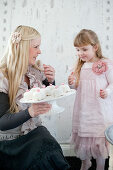 Festlich gekleidete Mutter mit kleiner Tochter eine Etagere mit Geburtstagsküchlein in der Hand haltend