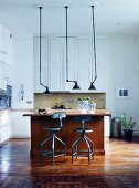 Vintage pendant lamps above wooden counter and bar stools in open-plan kitchen