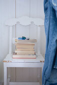 Stack of books on white-painted kitchen chair with carved back against white, wood-panelled wall