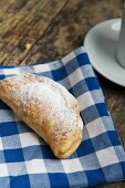 An apple turnover dusted with icing sugar on a checked cloth