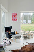 Grauer Ohrensessel im Fifiesstil mit Hocker und abgeschnittenen Baumstümpfen in modernem, weißem Wohnzimmer mit Gartenblick
