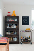 Dark wood display case next to portable bar on tea trolley in corner of modern dining room