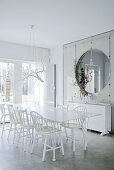 30s designer chairs around dining table and exposed concrete partition with round opening in white dining room