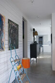 Stepladder below modern paintings on wood-clad wall and 70s lamp with orange lampshade