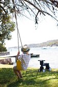 Summer idyll with back view of boy on swing; toddler's scooter and view of lake in blurred background