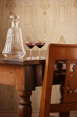 Antique glass decanter and glasses on wooden table and partially visible chair with carved back