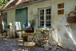 Gartenmöbel aus Eisen und nostalgische Blumenkörbe vor verwitterer Fassade