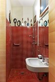 View into bathroom - red mosaic tiles in shower area and plain sink below mirror