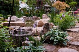 Große Natursteine und Gräser am Rande eines Gartenteichs und japanische Steinlampe im Hintergrund
