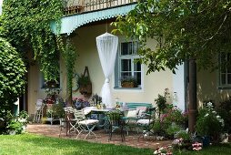 Seating area on terrace with delicate, shabby chic garden furniture in summer garden in front of old country house